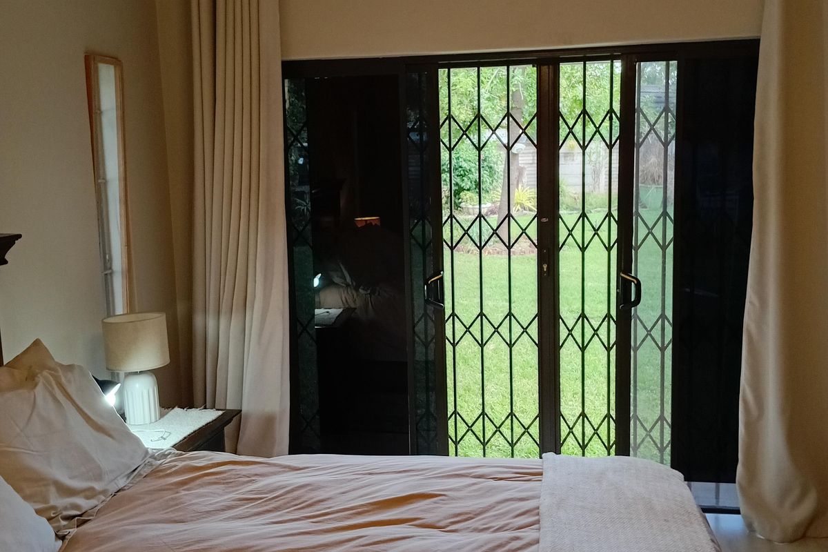 Bedroom featuring exposed timber ceiling beams and sliding glass doors with security gates, providing direct access to the garden.