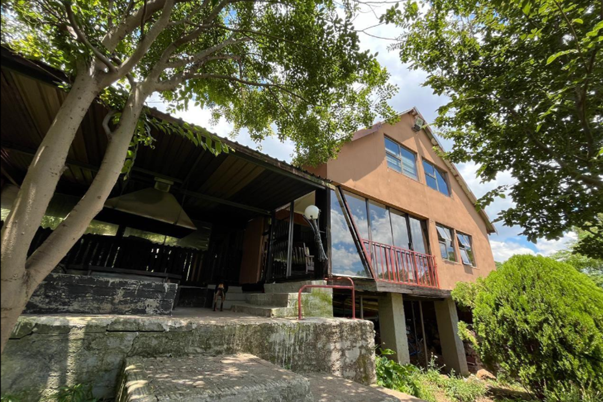 Exterior view of the rear of the house featuring a covered patio area, concrete stairs, and large windows with metal railings.