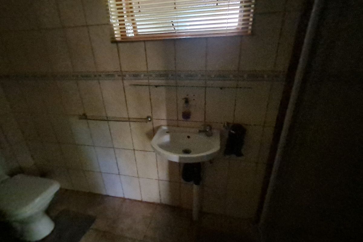 A dated bathroom featuring ceramic wall tiles, a wall-mounted basin, and a toilet, requiring modernization to improve functionality and aesthetic appeal.