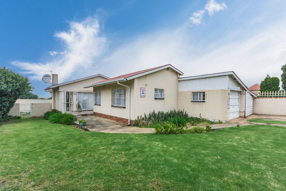 Rear view of the property featuring a lawn, concrete patio area, and attached garage with security bars on windows.