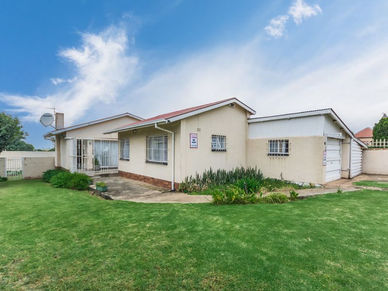 Rear view of the property featuring a lawn, concrete patio area, and attached garage with security bars on windows.