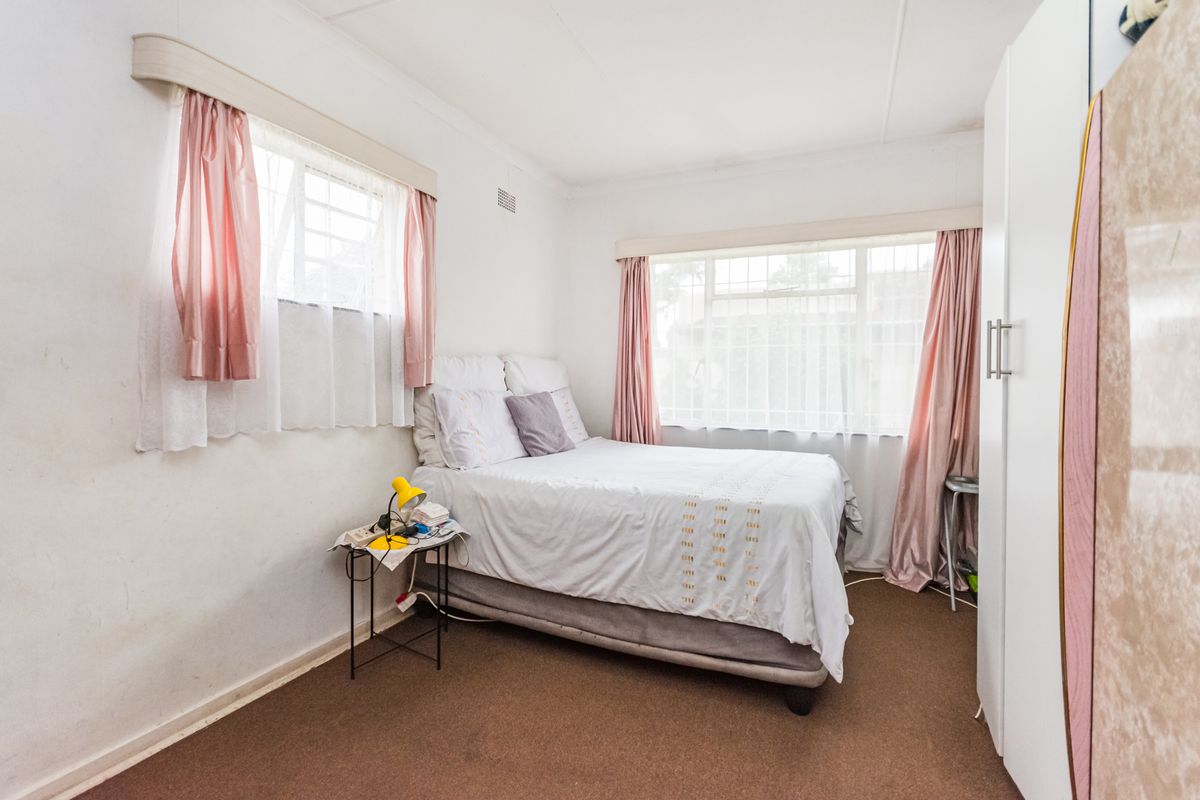 A functional bedroom featuring built-in wardrobe storage and dual windows with security bars, offering a bright space ready for cosmetic updates.