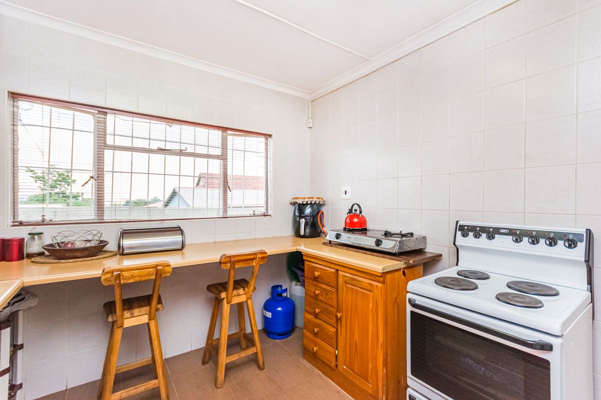 Functional kitchen featuring tiled walls, built-in wooden cabinetry, laminate countertops, and a freestanding stove, with security bars installed on the window.