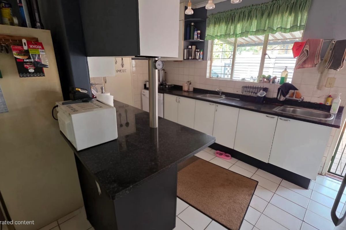 Functional kitchen featuring granite countertops, white cabinetry, a breakfast bar, and tiled flooring with a window overlooking the exterior.