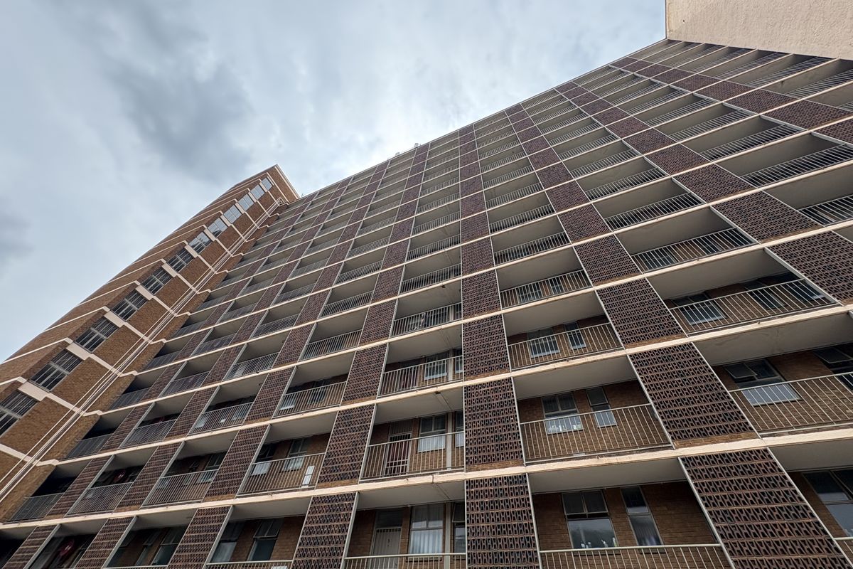 Low-angle view of a multi-story apartment building facade featuring repetitive balconies with metal railings and brick masonry construction.