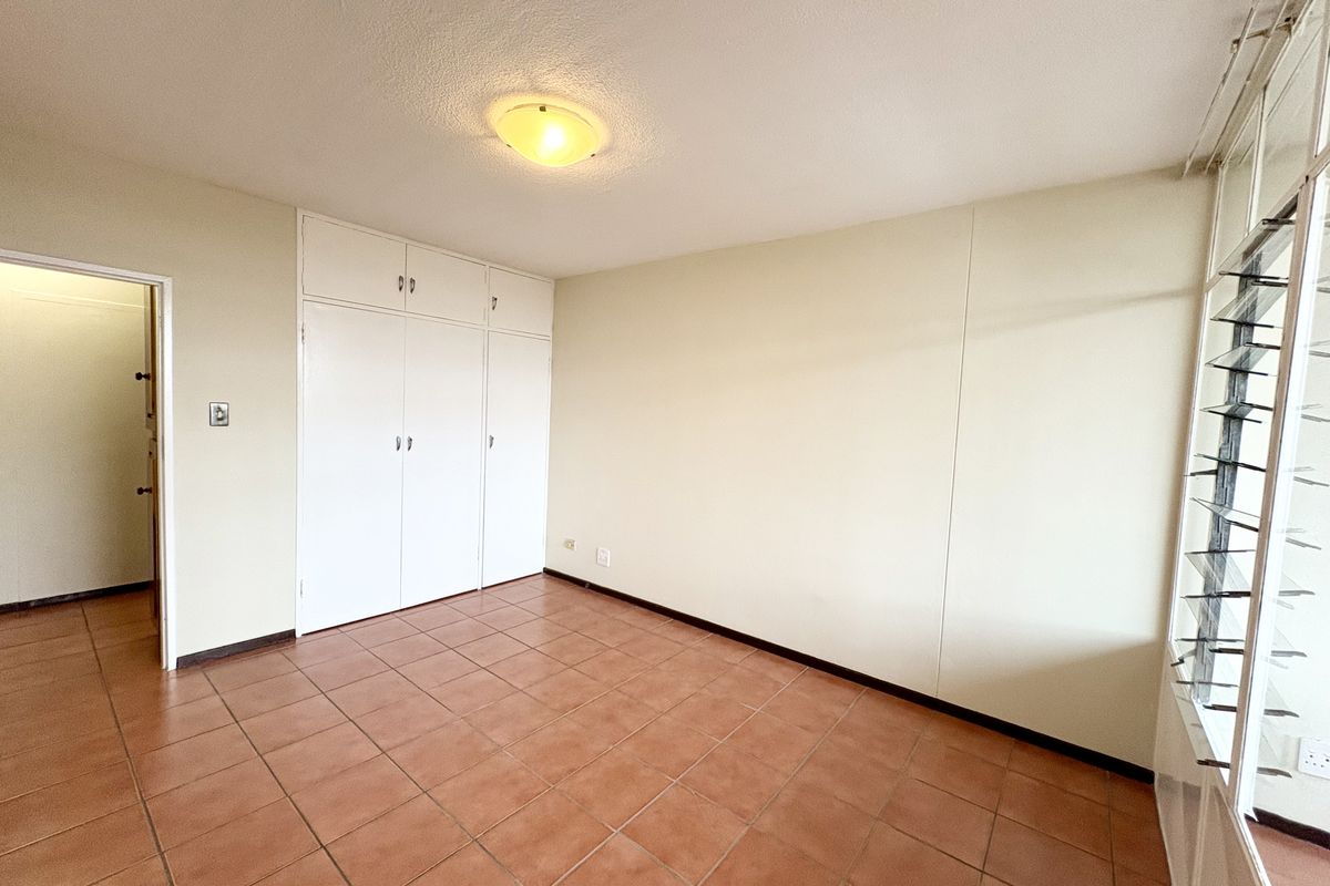 An empty bedroom featuring tiled flooring, built-in cupboards, and louvered windows, offering a blank canvas for potential interior updates.