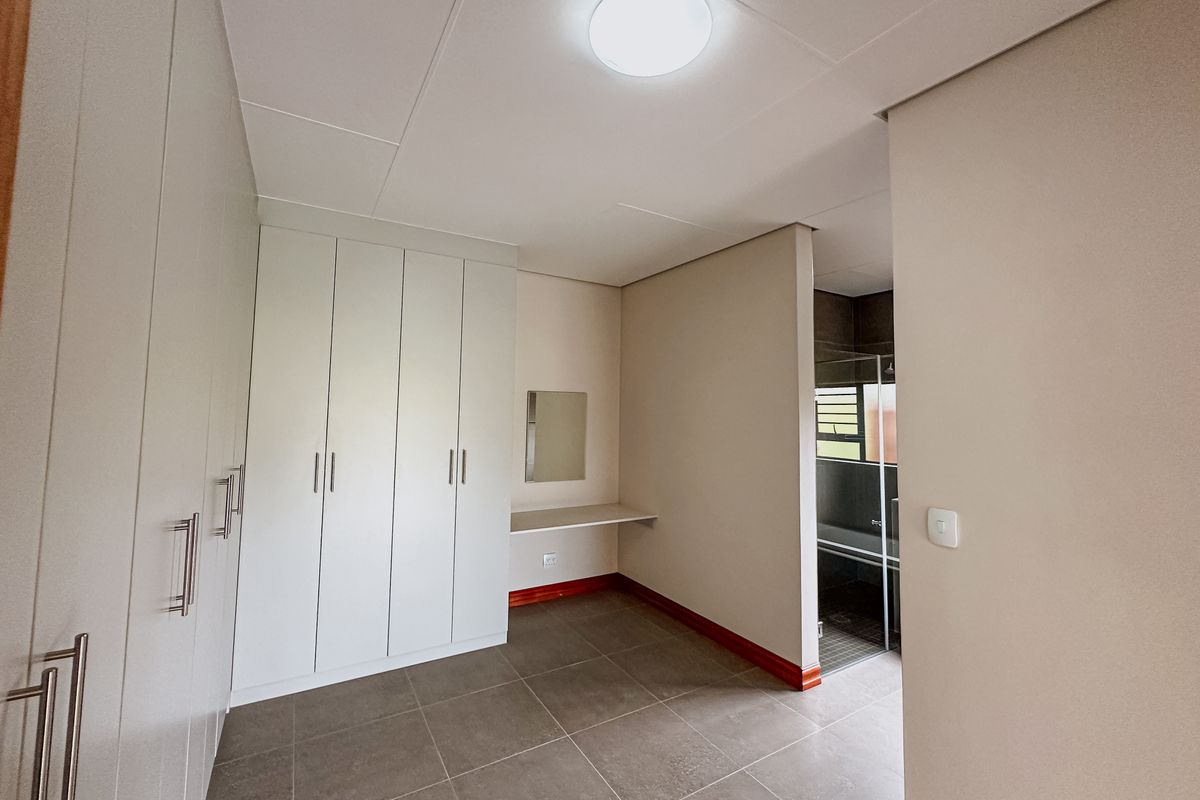 A clean, modern bedroom area featuring extensive built-in cupboards, tiled flooring, a floating vanity shelf, and direct access to an en-suite bathroom.