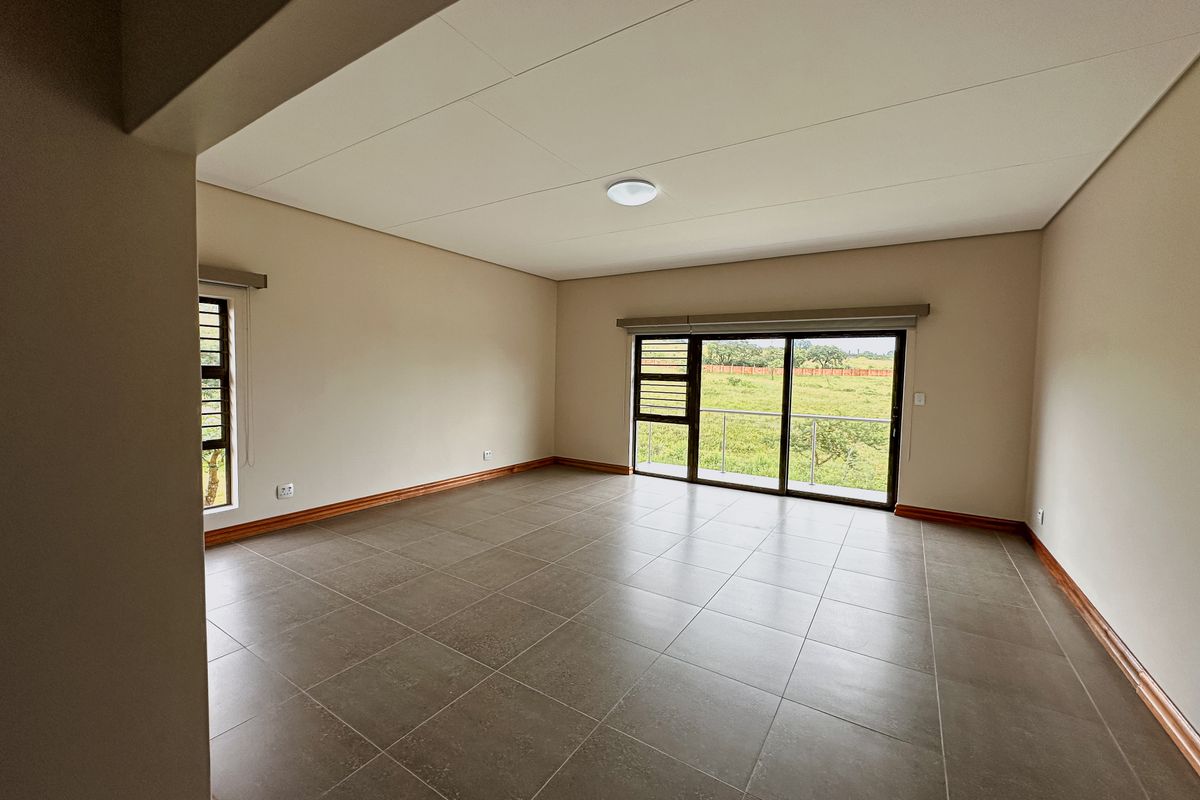 A spacious, empty living area featuring neutral tiled floors, large sliding glass doors leading to a balcony, and ample natural light.