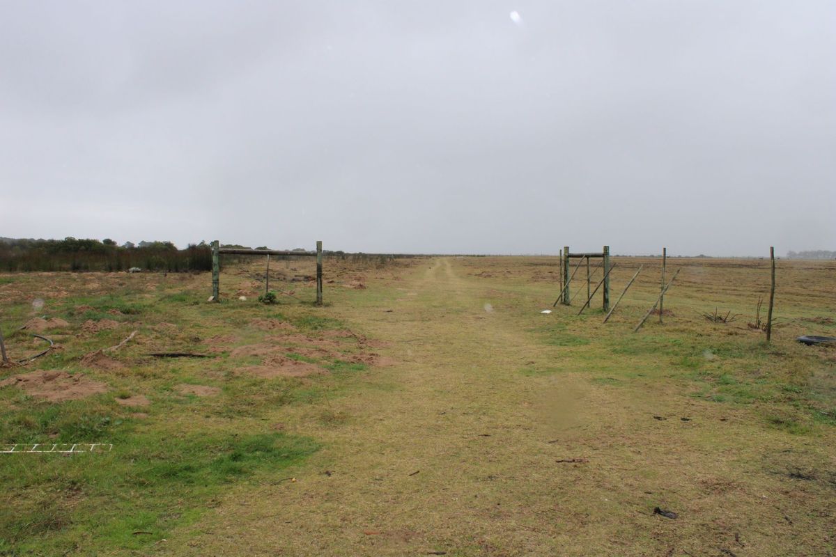 Expansive open farm land featuring a dirt track path and basic timber post and wire fencing.