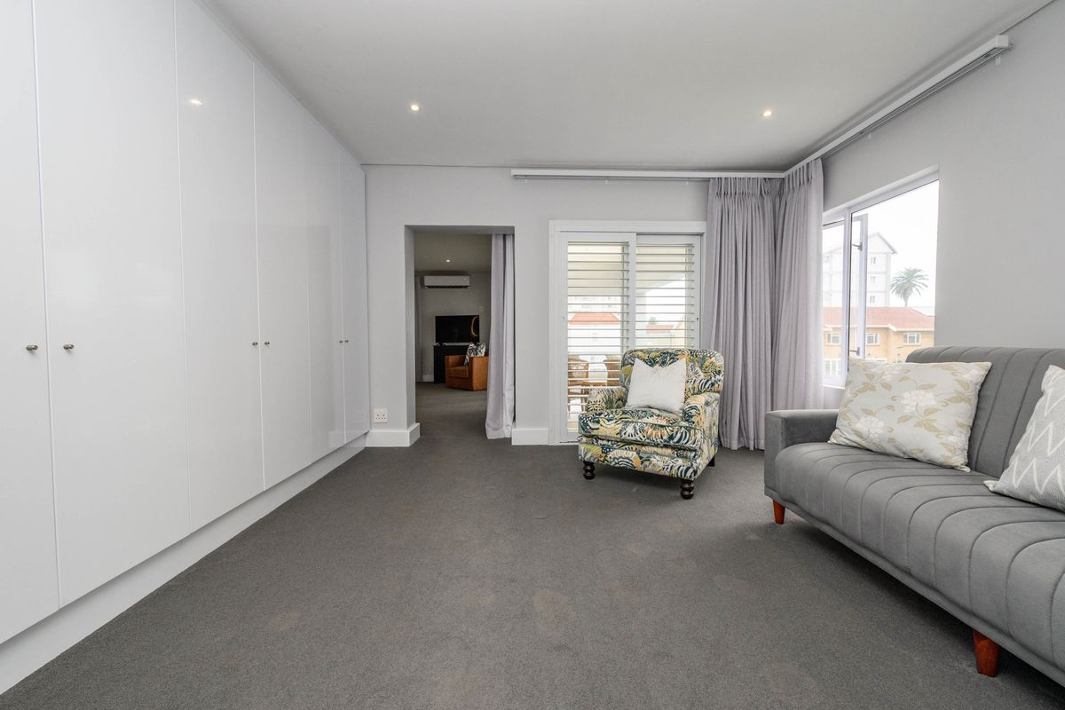 A well-maintained bedroom featuring extensive built-in cupboards, neutral carpeting, and direct access to an outdoor balcony through sliding glass doors.