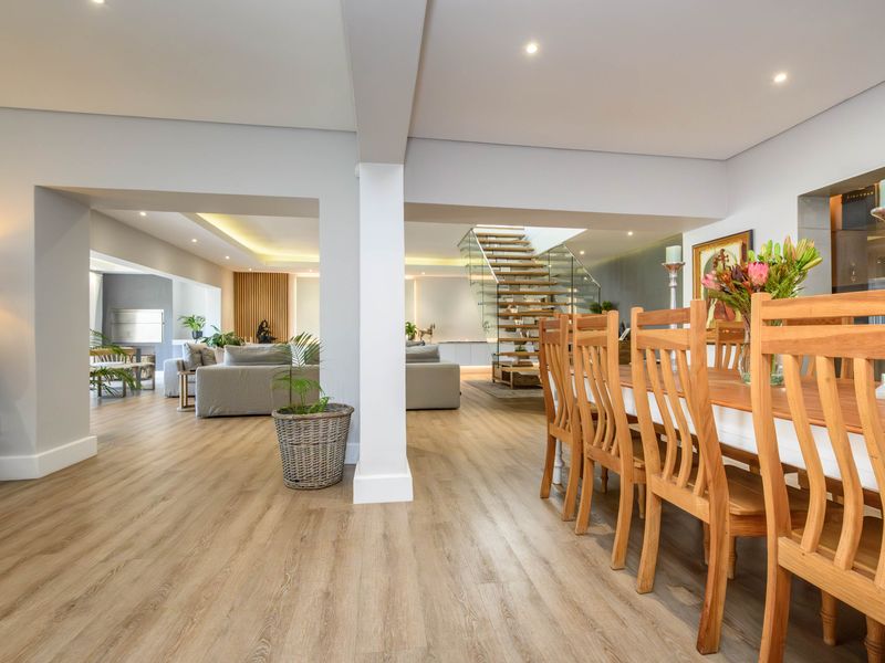 Spacious open-plan living and dining area featuring modern laminate flooring, recessed lighting, and a striking timber staircase with a glass balustrade.