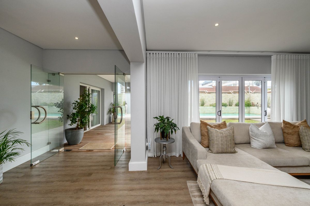 Modern living area featuring high-quality laminate flooring, recessed lighting, and seamless access to the outdoor patio through frameless glass pivot and bi-fold doors.