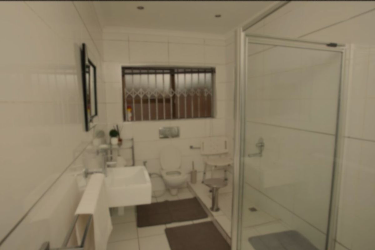 A functional bathroom featuring a glass-enclosed shower, wall-mounted basin, and toilet, finished with white wall tiles and tiled flooring.