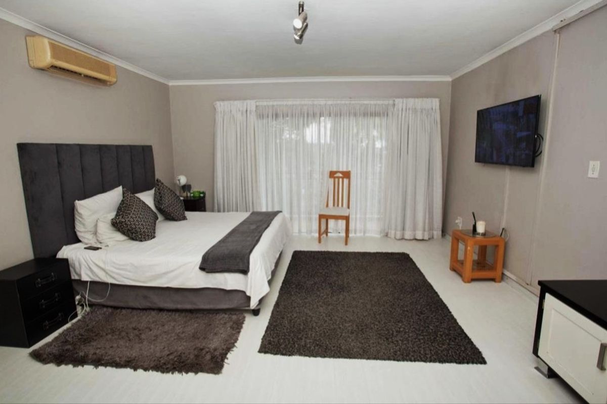 Spacious bedroom featuring light-toned flooring, a wall-mounted air conditioning unit, and large sliding glass doors with curtains leading to the exterior.