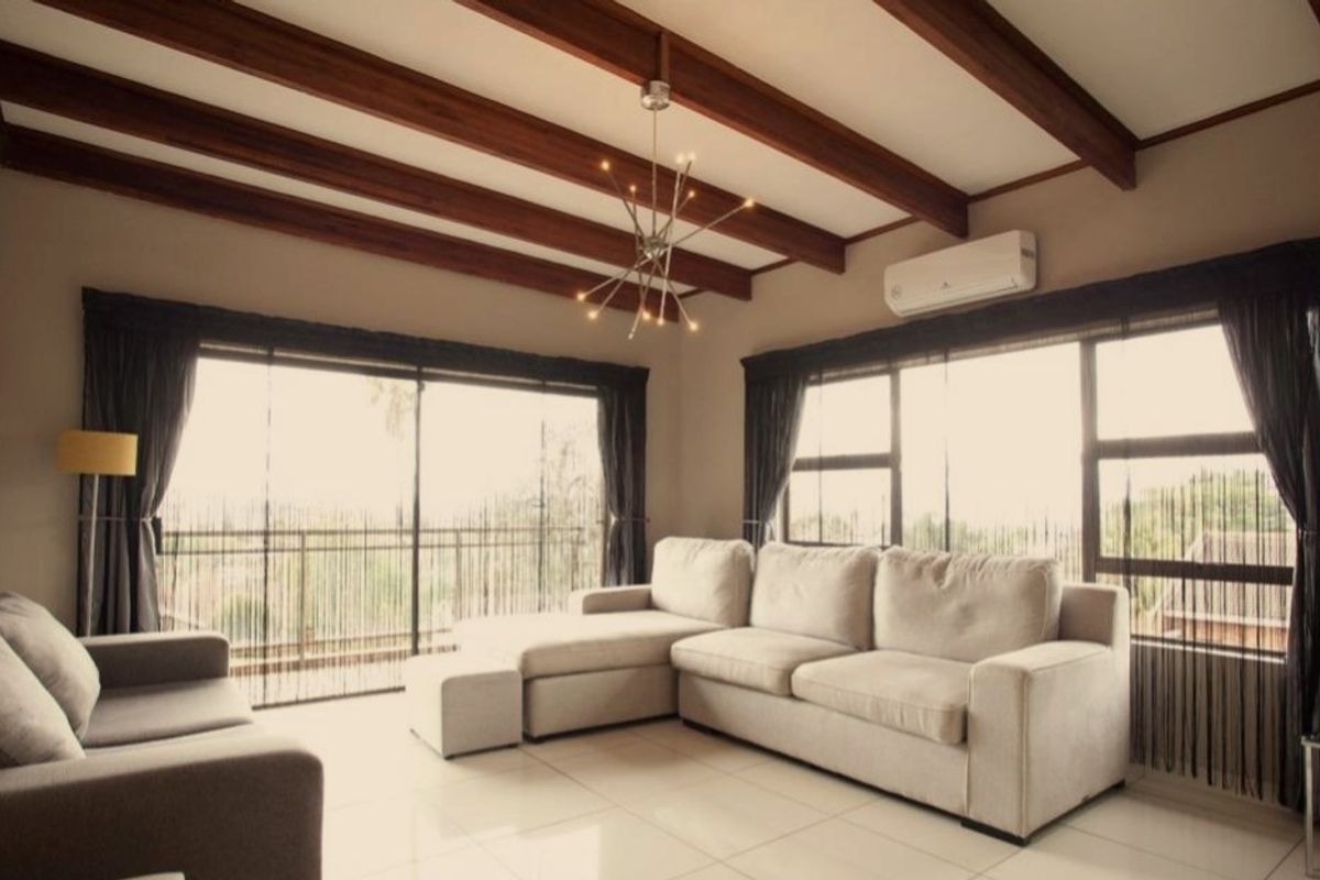 A bright living room featuring exposed timber ceiling beams, large windows with natural light, and a wall-mounted air conditioning unit.