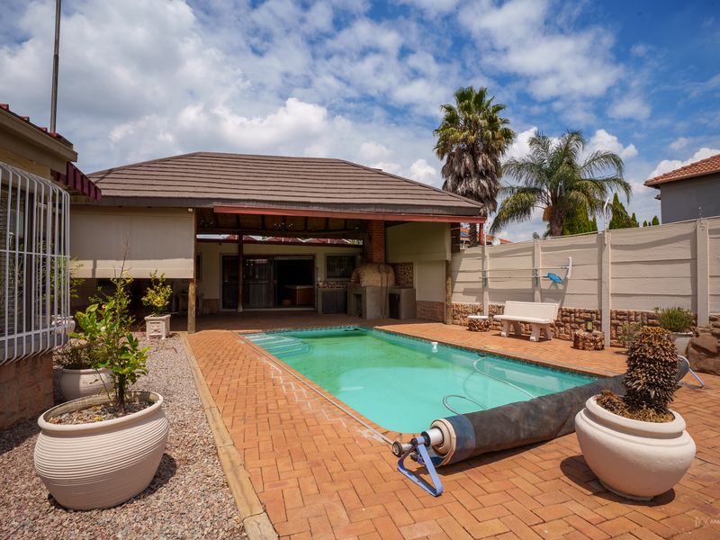 Outdoor pool area featuring a covered patio with a built-in pizza oven, brick paving, and perimeter walling.