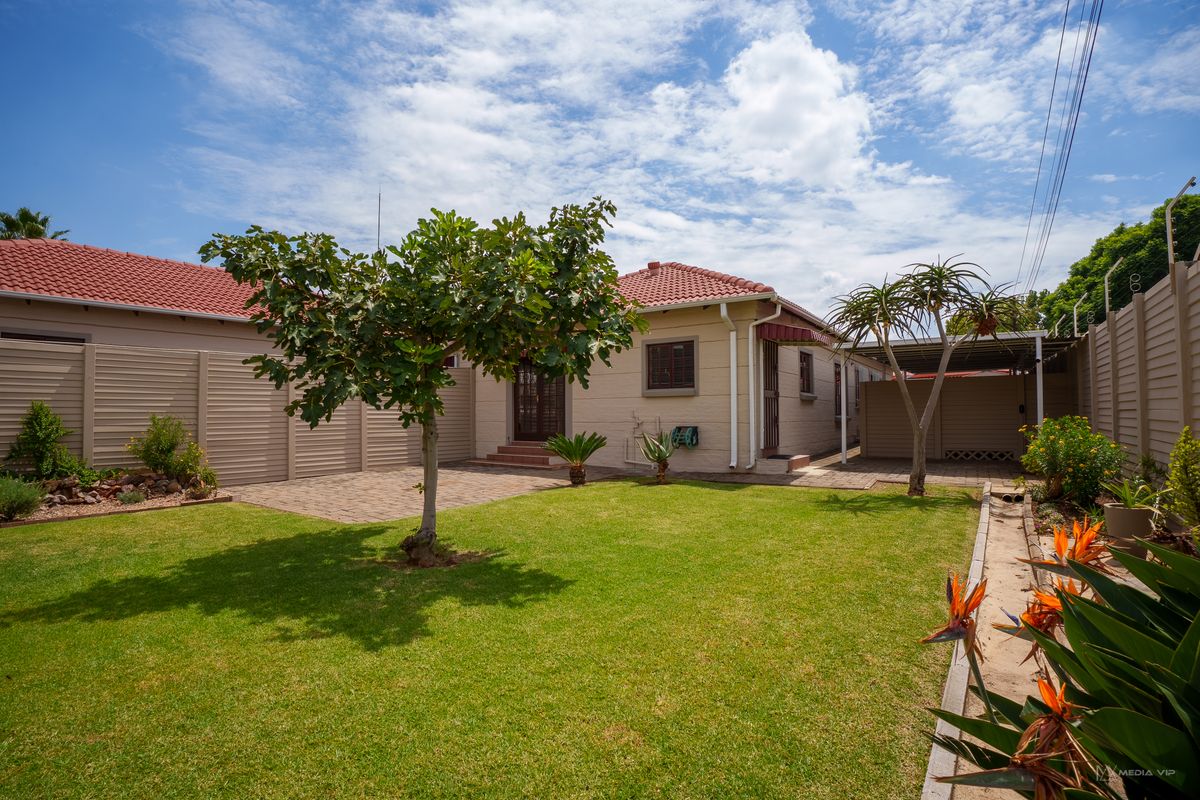 A well-maintained rear garden featuring a paved patio area, a neat lawn, and a covered carport, enclosed by secure perimeter fencing.