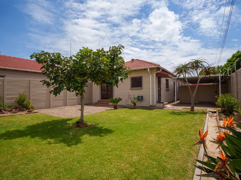 A well-maintained rear garden featuring a paved patio area, a neat lawn, and a covered carport, enclosed by secure perimeter fencing.