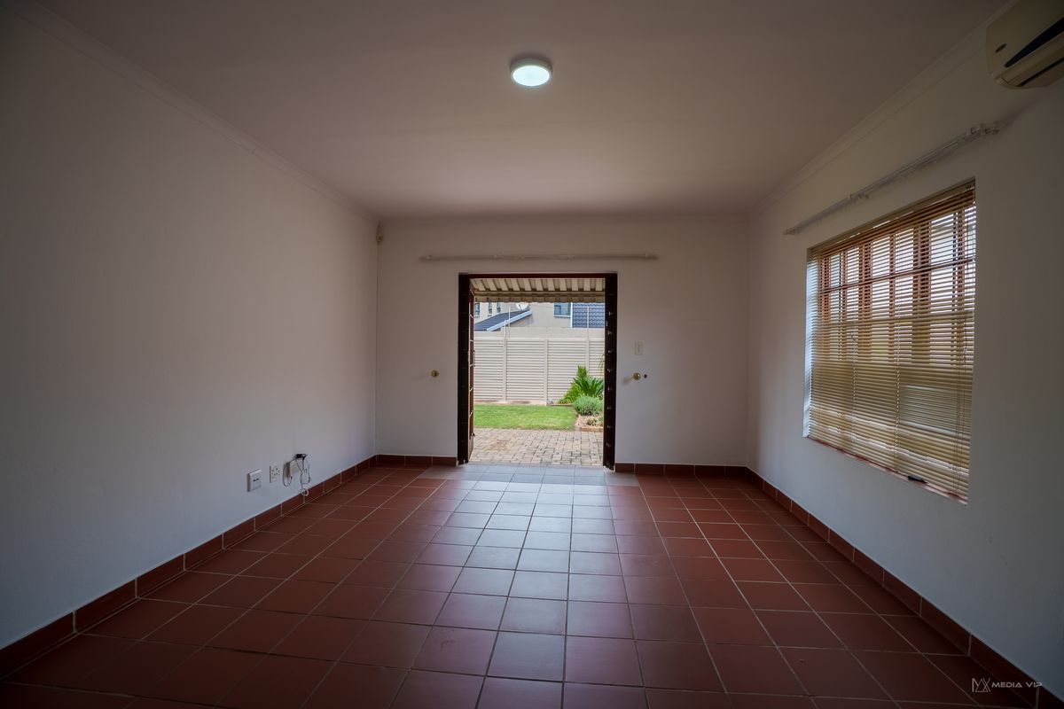 An empty living room featuring ceramic tile flooring, venetian blinds, and an air conditioning unit, with direct access to the rear garden.