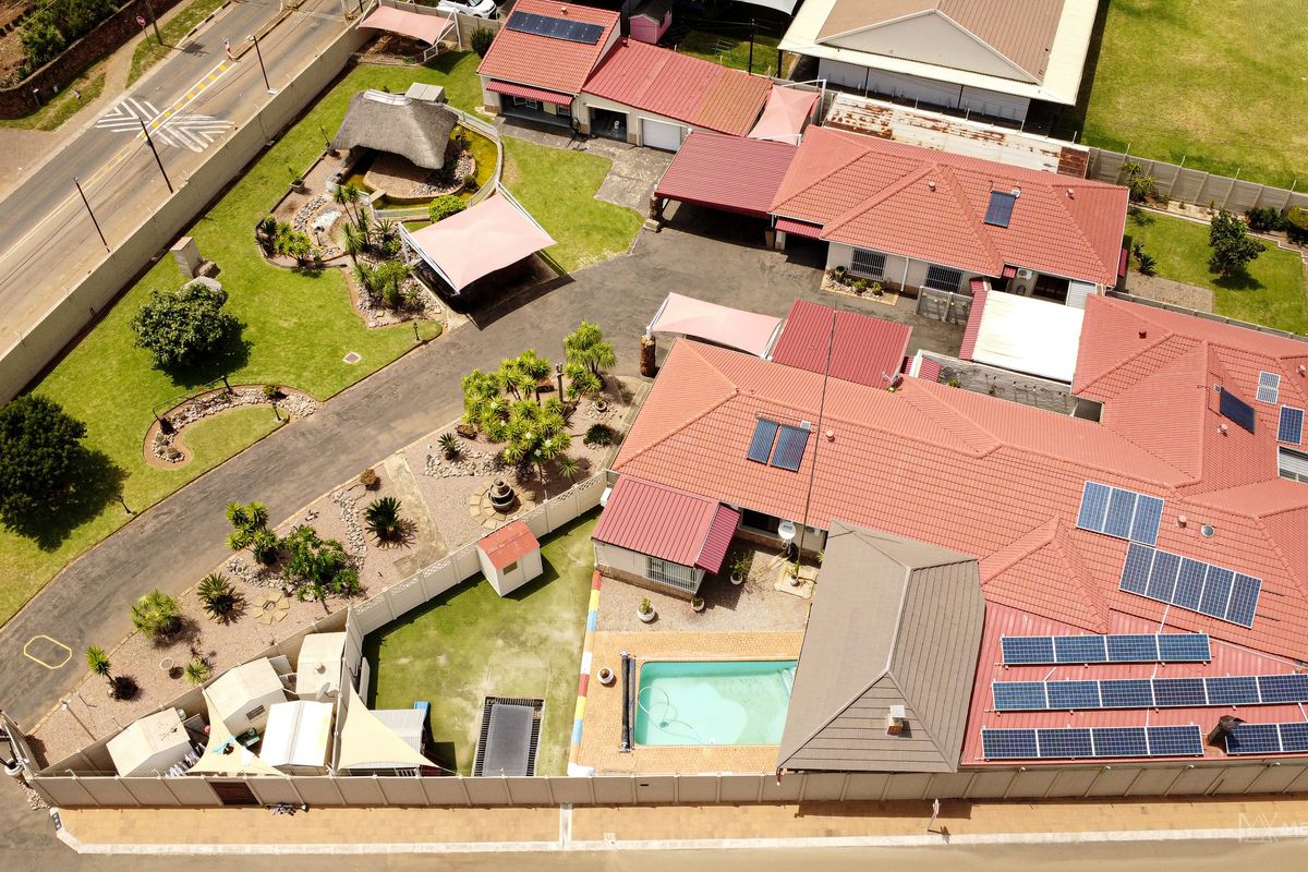 Aerial view of the property featuring a large tiled roof with solar panels, a swimming pool, landscaped garden, and a detached thatched lapa.