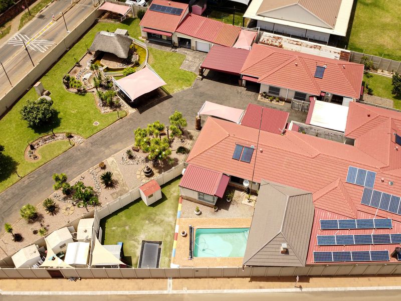 Aerial view of the property featuring a large tiled roof with solar panels, a swimming pool, landscaped garden, and a detached thatched lapa.