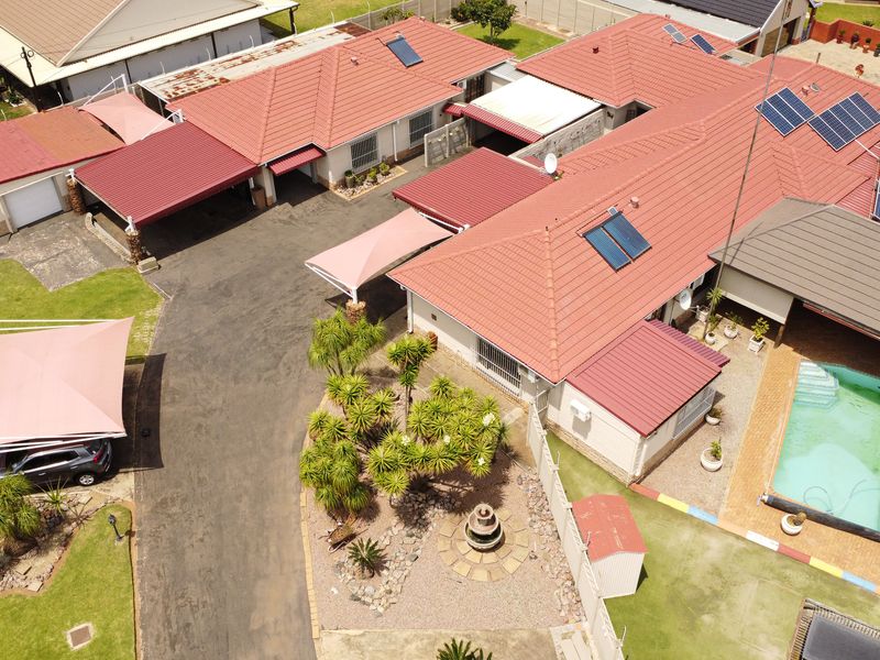Aerial view of a residential property featuring a tiled roof with solar installations, a swimming pool, paved driveway, and established garden areas.