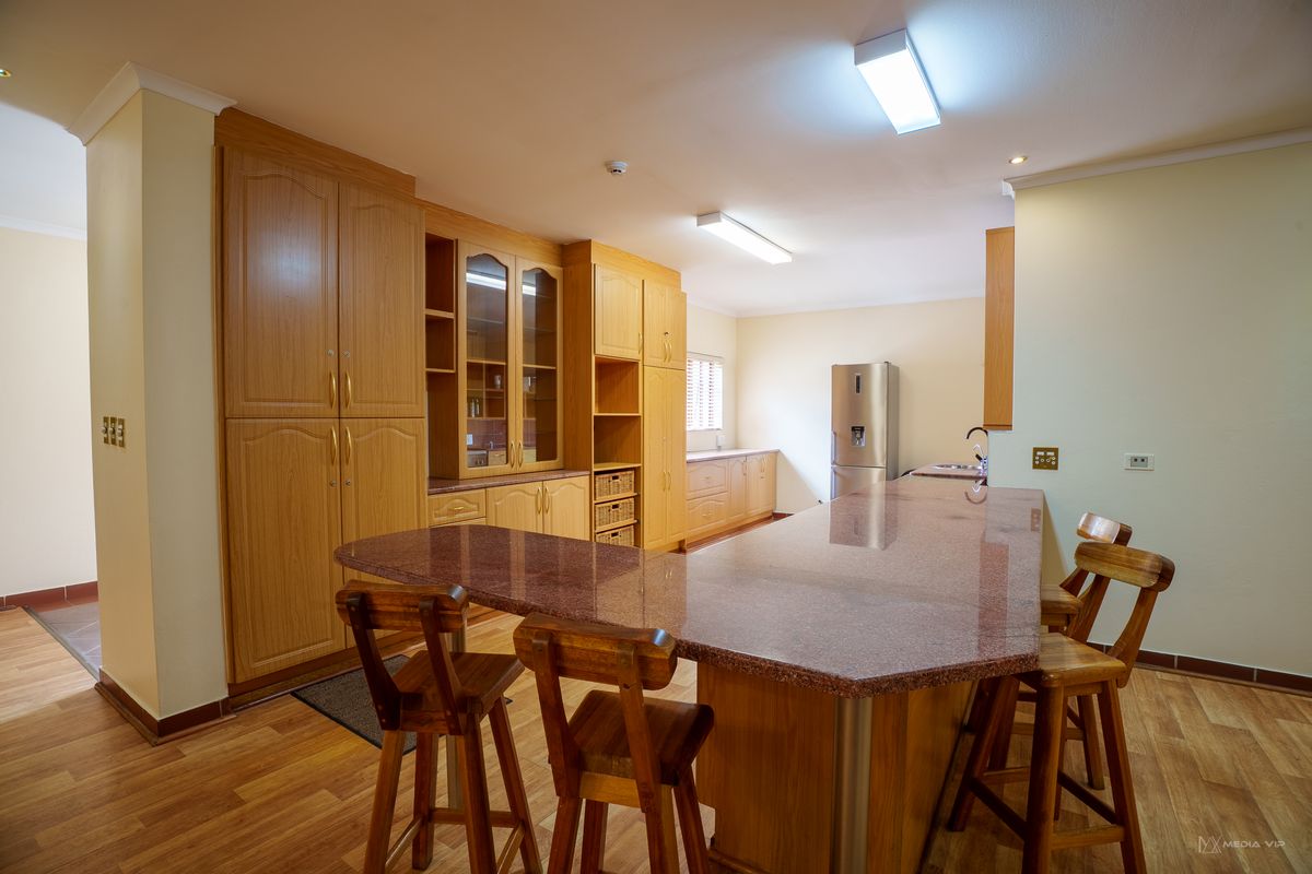 Spacious kitchen featuring extensive wooden cabinetry, a large granite-topped breakfast bar, and functional layout with integrated storage solutions.