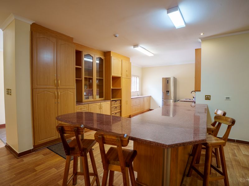 Spacious kitchen featuring extensive wooden cabinetry, a large granite-topped breakfast bar, and functional layout with integrated storage solutions.