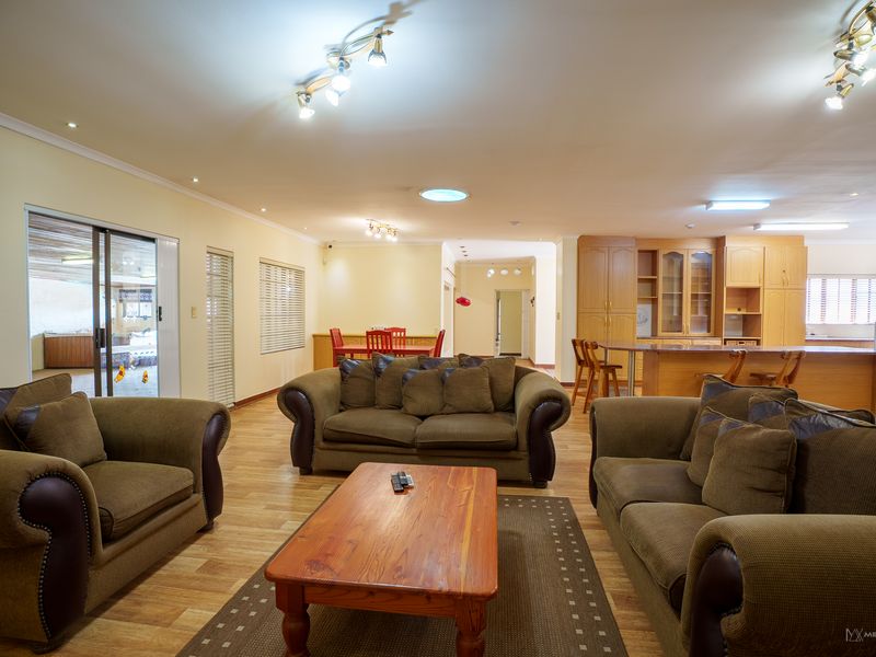 Spacious open-plan living area featuring laminate flooring, a large kitchen with built-in cabinetry, and sliding doors leading to an outdoor patio space.