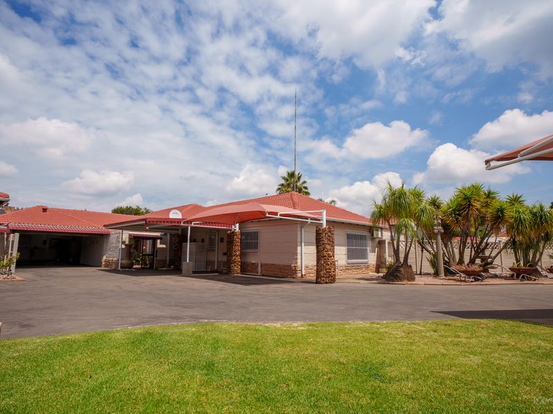 Front exterior view of the house featuring a large asphalt driveway, covered carport area, tiled roof, and landscaped garden.