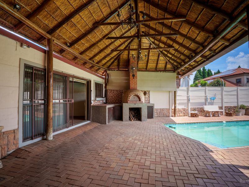 Spacious covered patio featuring a thatched roof, exposed timber trusses, and a built-in brick pizza oven, overlooking a private swimming pool.