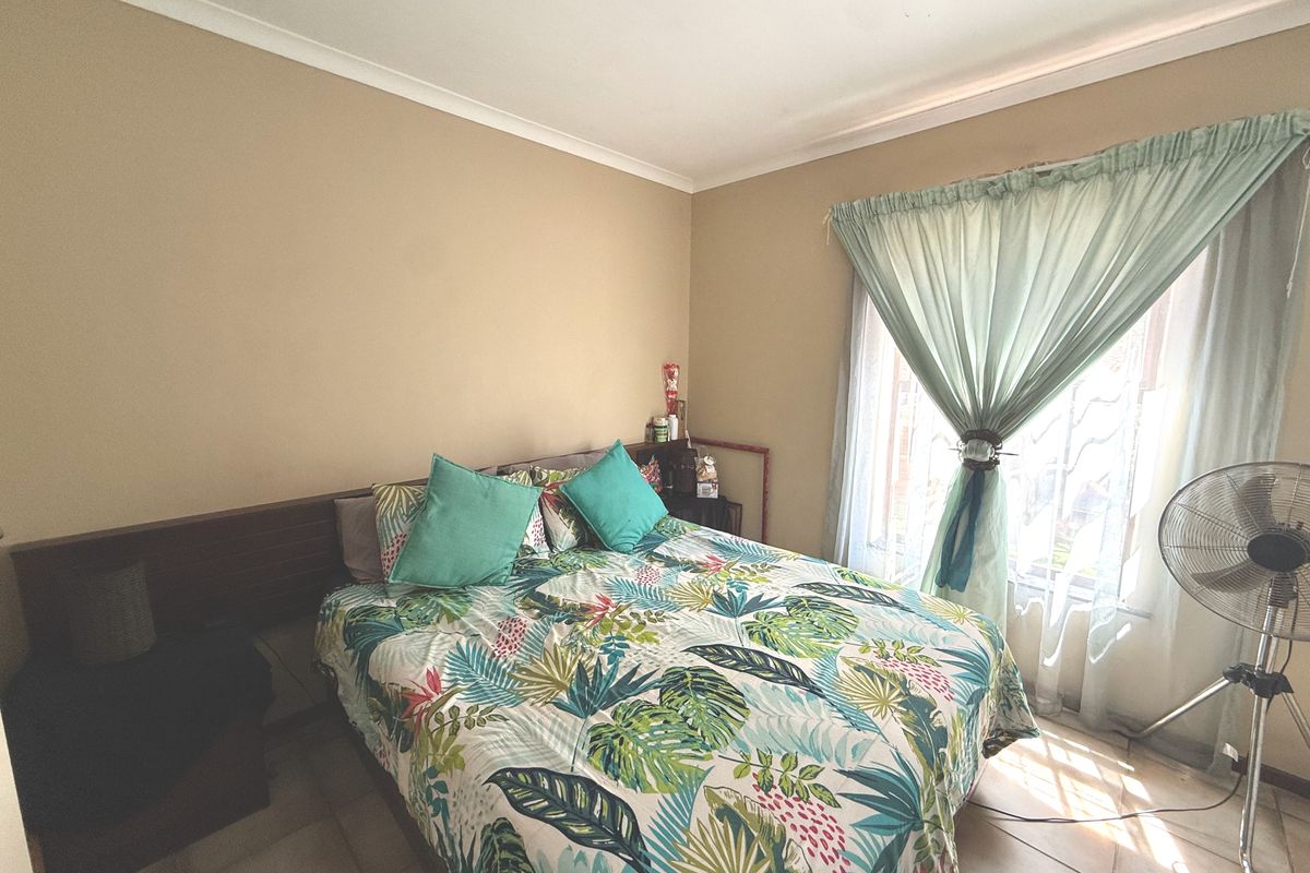 A bedroom featuring tiled flooring, a built-in headboard, and a window with curtain treatments.