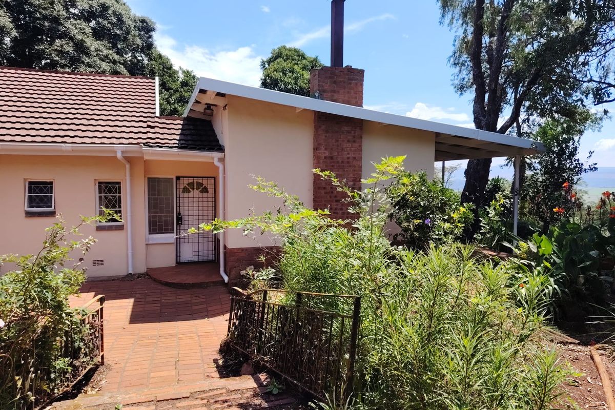Rear exterior view of the house featuring a brick chimney, tiled roof, and paved patio area surrounded by established garden greenery.