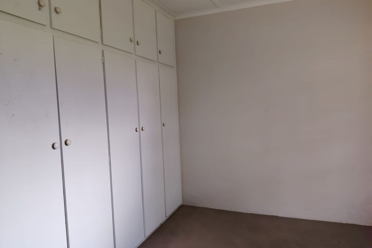 An empty bedroom featuring extensive built-in storage cupboards and carpeted flooring, offering a blank canvas for potential updates and interior design.