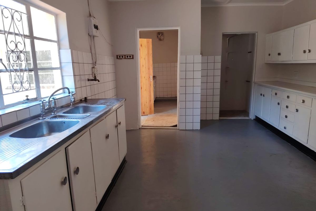 A functional kitchen space featuring built-in cabinetry, a double stainless steel sink, and tiled splashbacks, offering a blank canvas for potential renovation.
