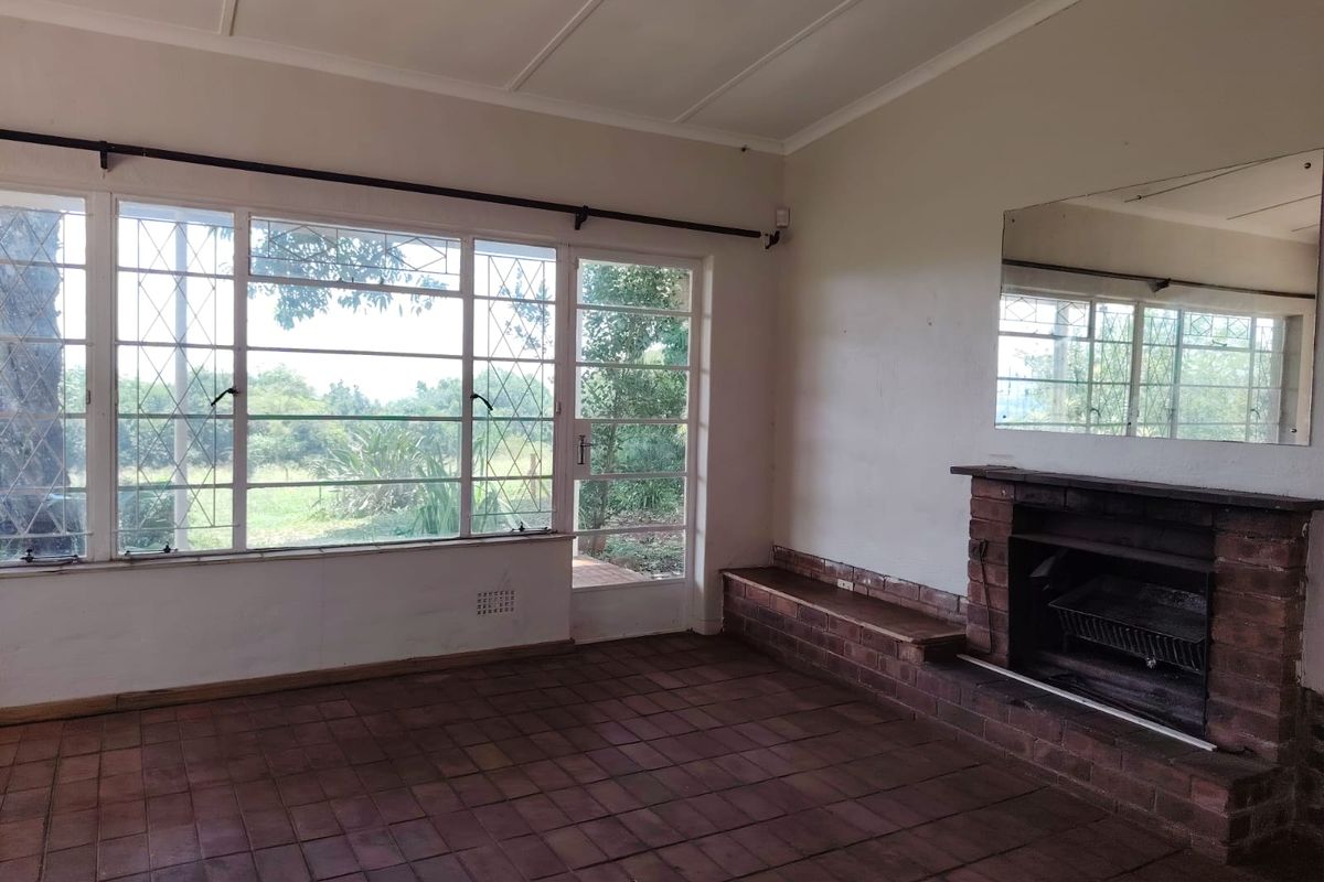 Spacious living room featuring a traditional brick fireplace, terracotta tile flooring, and large steel-framed windows providing natural light and garden views.