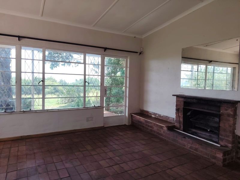 Spacious living room featuring a traditional brick fireplace, terracotta tile flooring, and large steel-framed windows providing natural light and garden views.