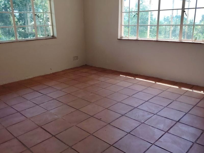 A bright, empty living room featuring terracotta floor tiles and large steel-framed windows, offering a blank canvas for interior design.