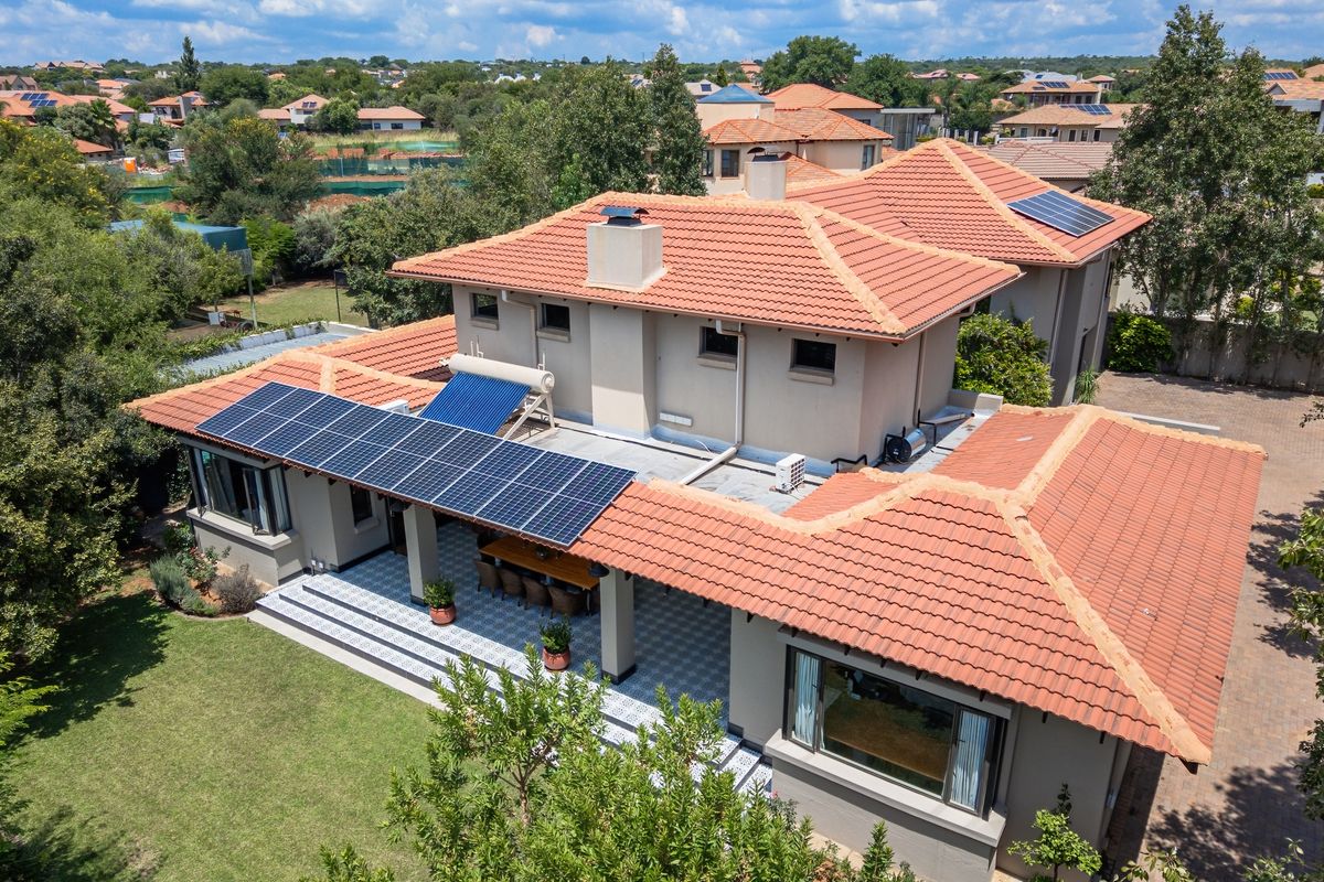 Aerial view of a residential property featuring a tiled roof, integrated solar panels, solar water heating system, and a spacious covered patio area.
