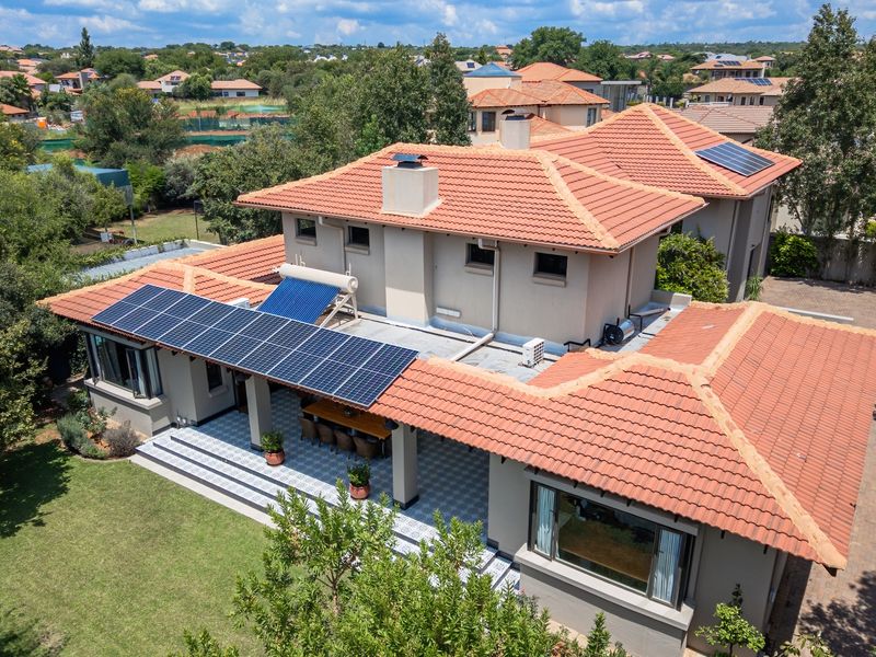 Aerial view of a residential property featuring a tiled roof, integrated solar panels, solar water heating system, and a spacious covered patio area.