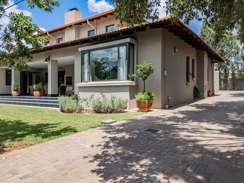 Rear view of the house featuring a covered patio, brick paved driveway, and a well-maintained garden with a bay window.