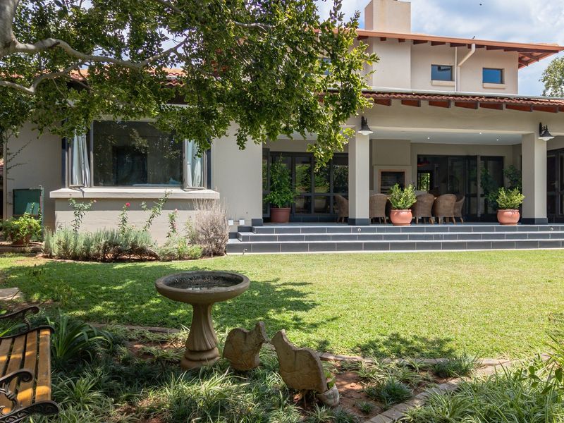 Rear view of the house featuring a spacious tiled patio, landscaped garden, and large sliding glass doors leading into the living area.