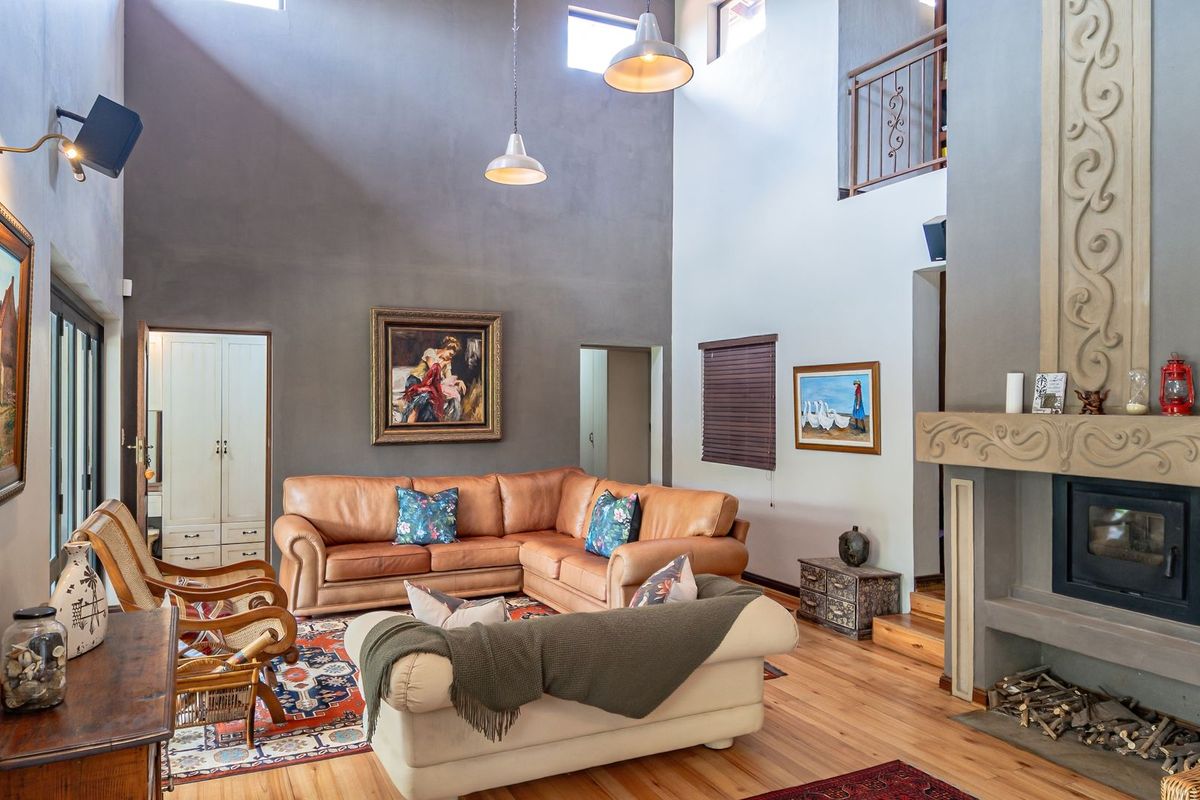 Spacious double-volume living room featuring a prominent fireplace with a wood-burning stove, hardwood flooring, and an open mezzanine level overlooking the area.