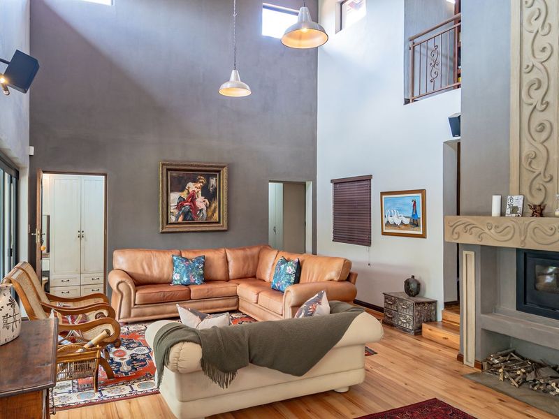 Spacious double-volume living room featuring a prominent fireplace with a wood-burning stove, hardwood flooring, and an open mezzanine level overlooking the area.