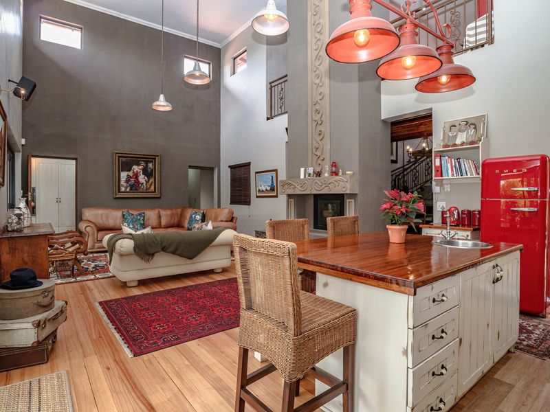 Spacious open-plan living area featuring high ceilings, a central kitchen island, a prominent fireplace, and a mezzanine level with wrought iron detailing.