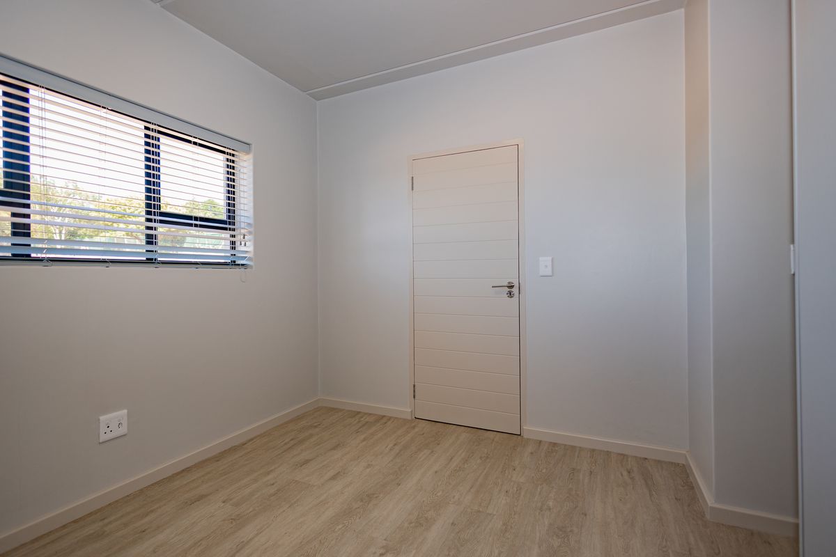 A clean, empty bedroom featuring light-toned laminate flooring, a modern internal door, and a window fitted with horizontal blinds.