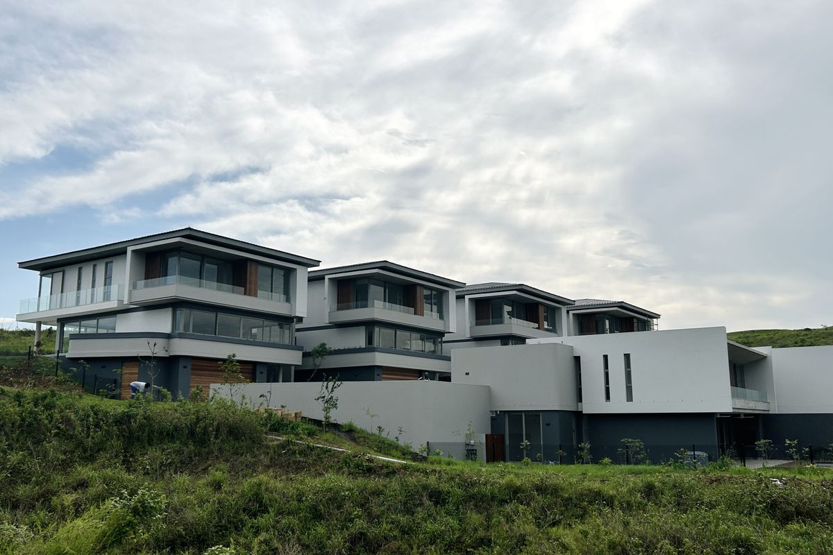 A modern multi-level townhouse complex featuring contemporary architectural design, glass balustrades, and clean exterior finishes set against a landscaped hillside.