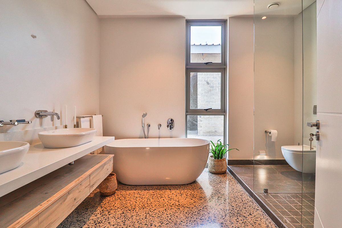 Modern bathroom featuring a freestanding bathtub, double vanity with wall-mounted faucets, walk-in shower with glass screen, and wall-hung toilet on terrazzo flooring.