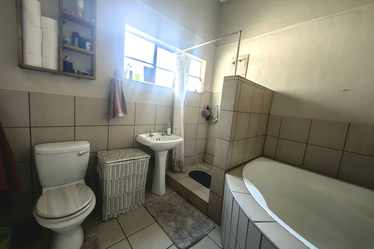 A functional bathroom featuring a pedestal basin, toilet, built-in bathtub, and a tiled shower enclosure with neutral wall and floor tiling.