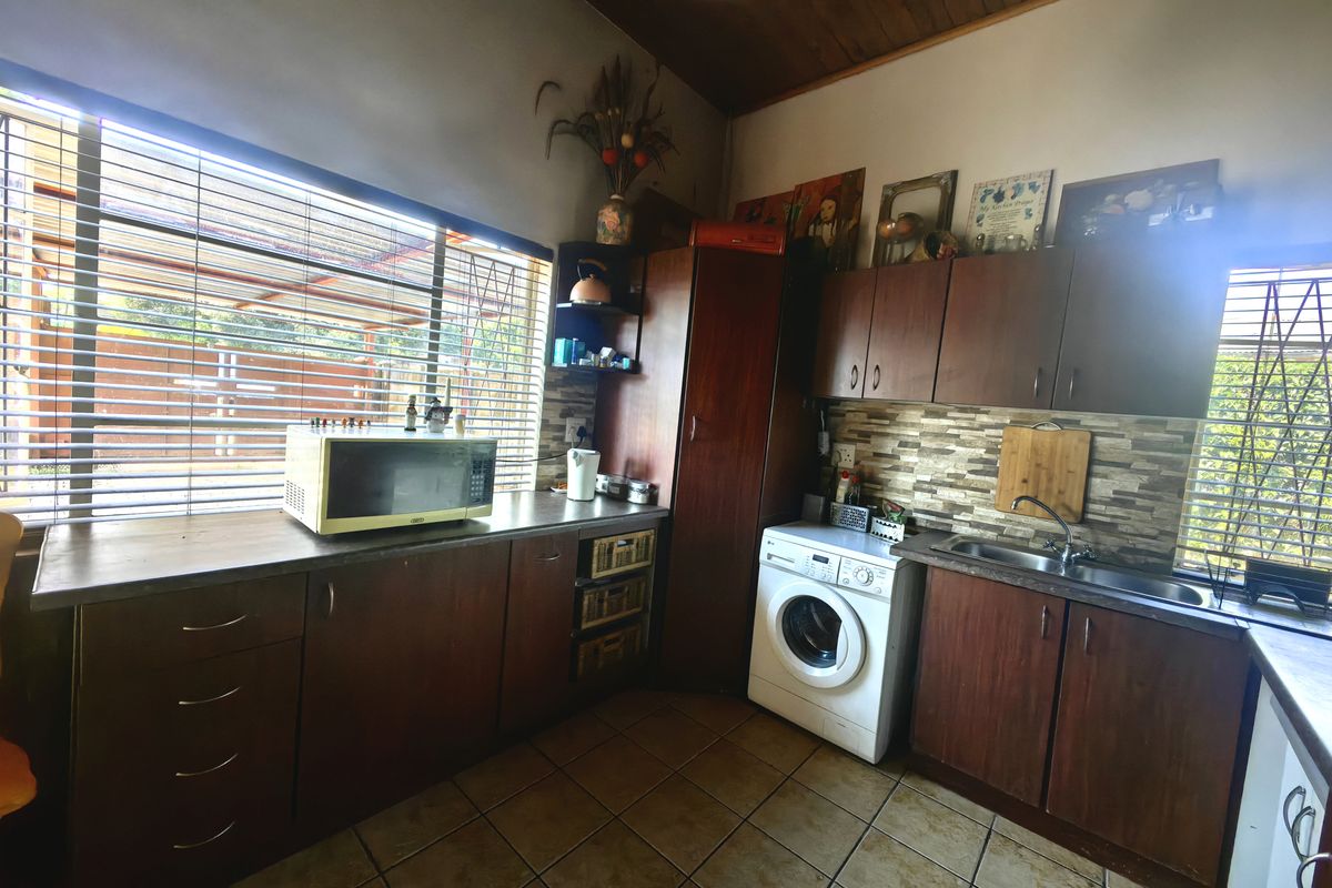 A functional kitchen featuring dark wood cabinetry, stone-look tile backsplash, ceramic floor tiles, and a timber-paneled ceiling with integrated laundry plumbing.